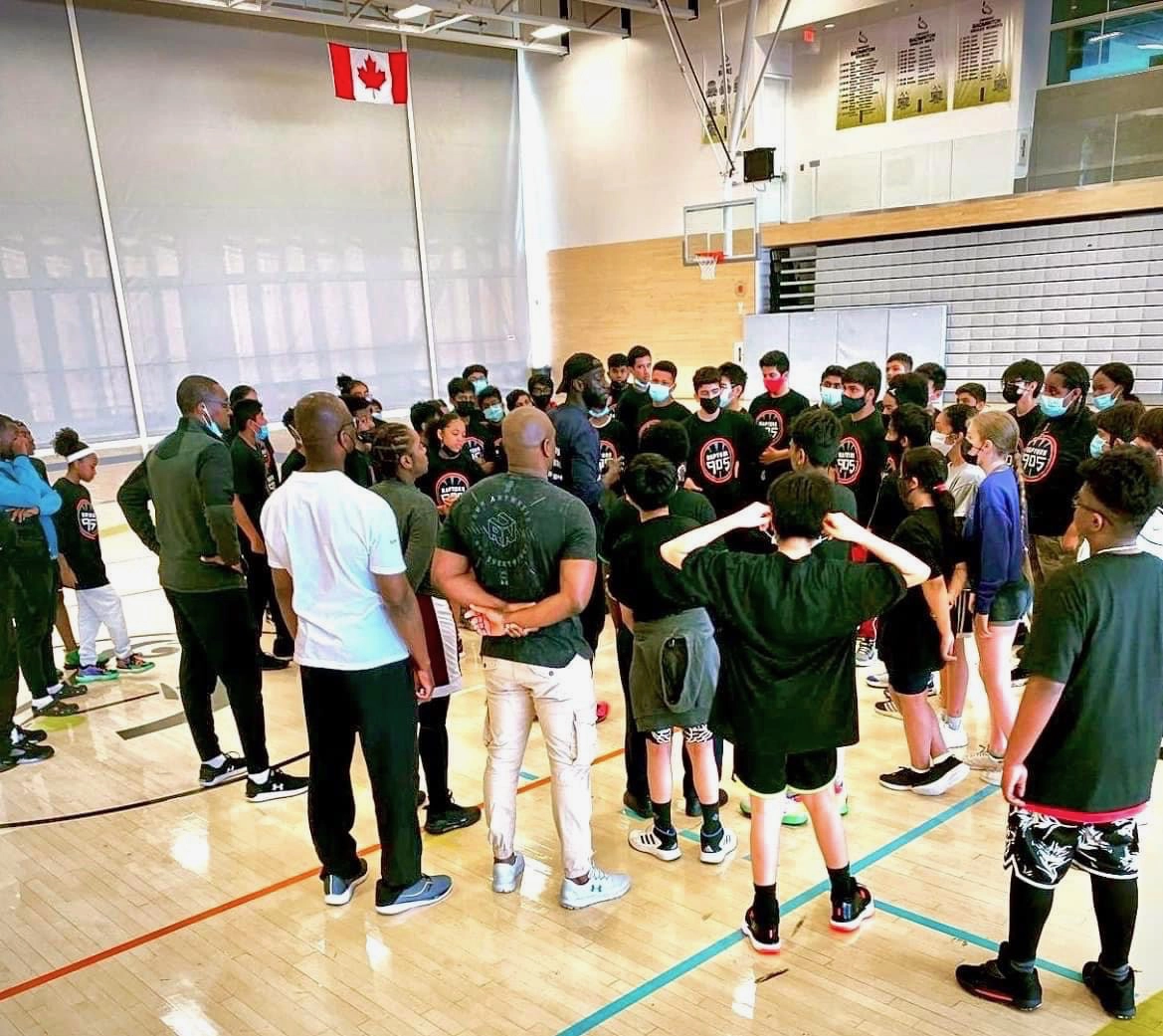 Coaches speaking with a large group of young athletes in a gym.